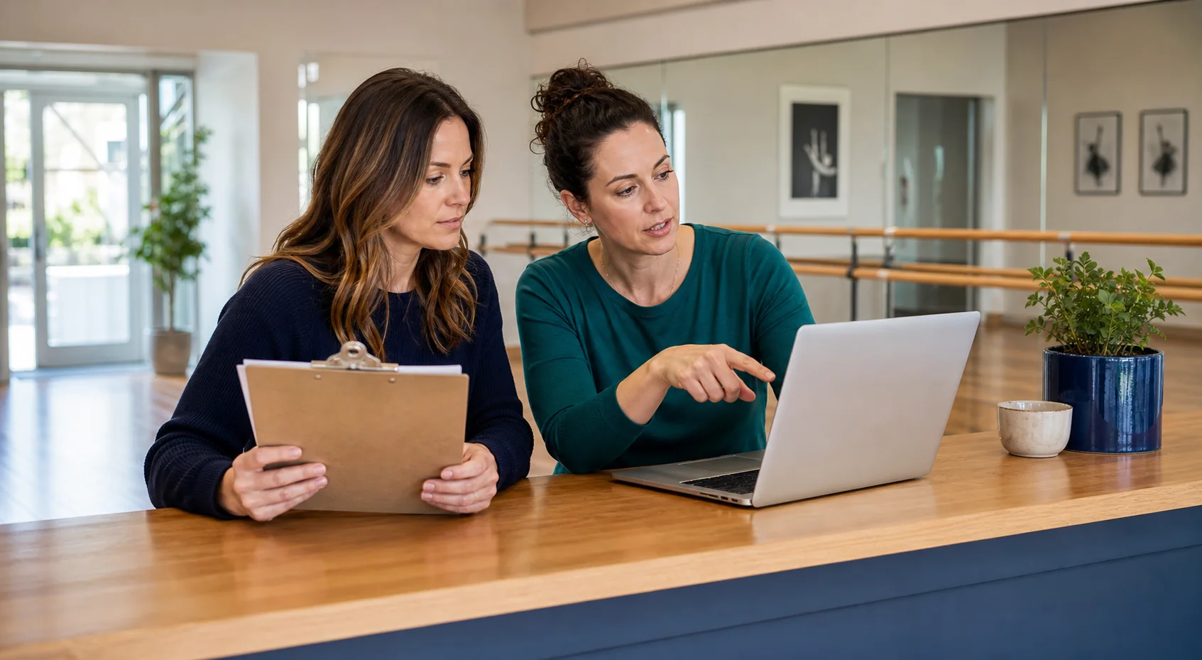 Two dance studio managers comparing software at a laptop and clipboard