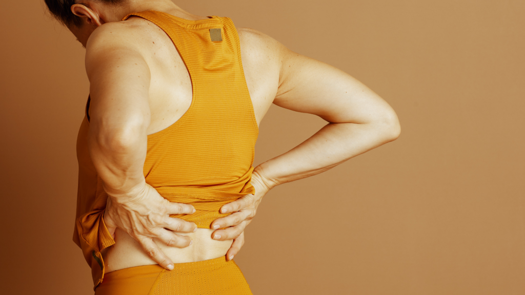 A person placing both hands on their lower back, showing signs of discomfort from back pain.